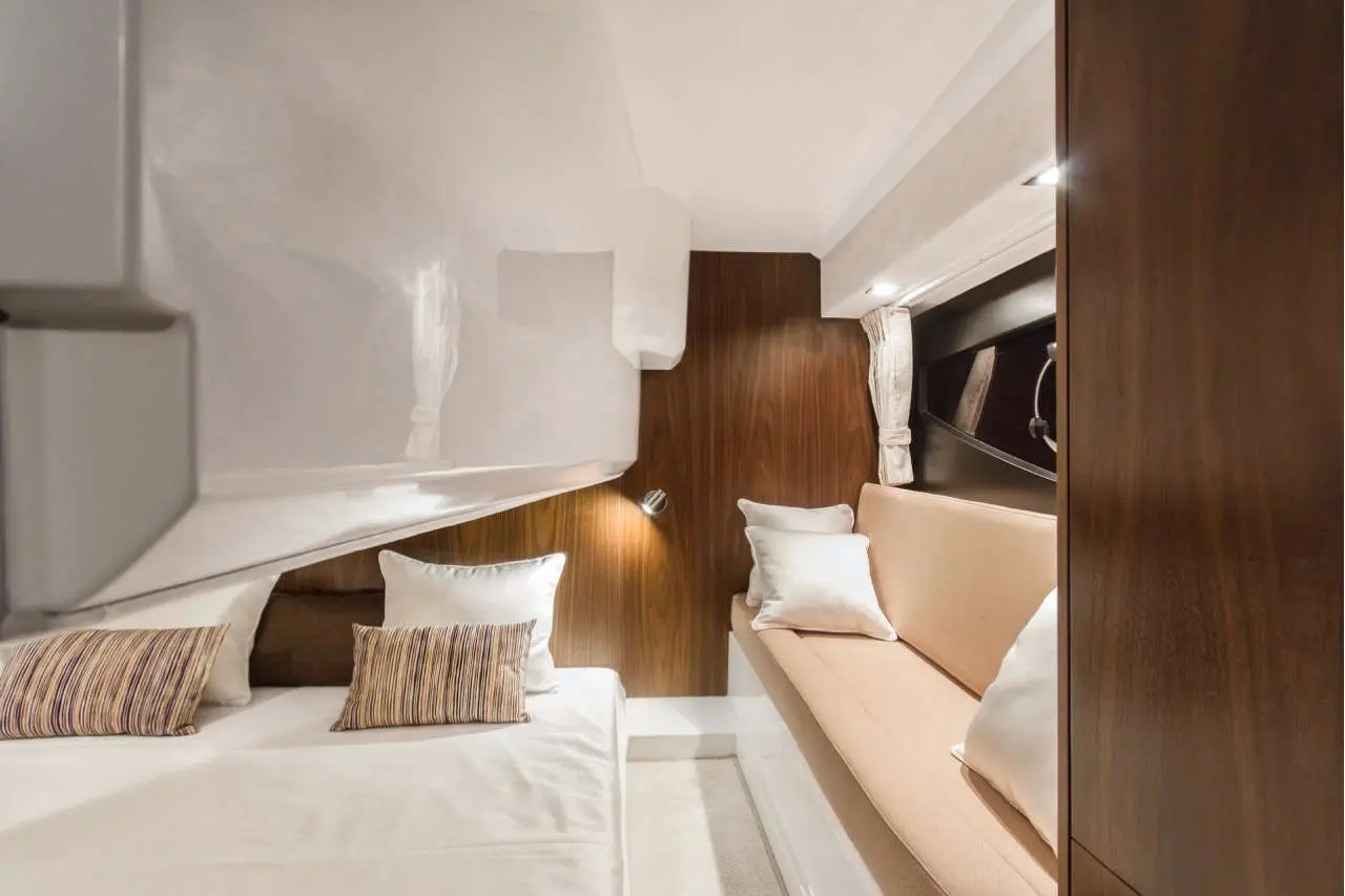 Modern cabin interior with a double bed, beige sofa, white cushions, and wooden accents, creating a stylish nautical atmosphere.
