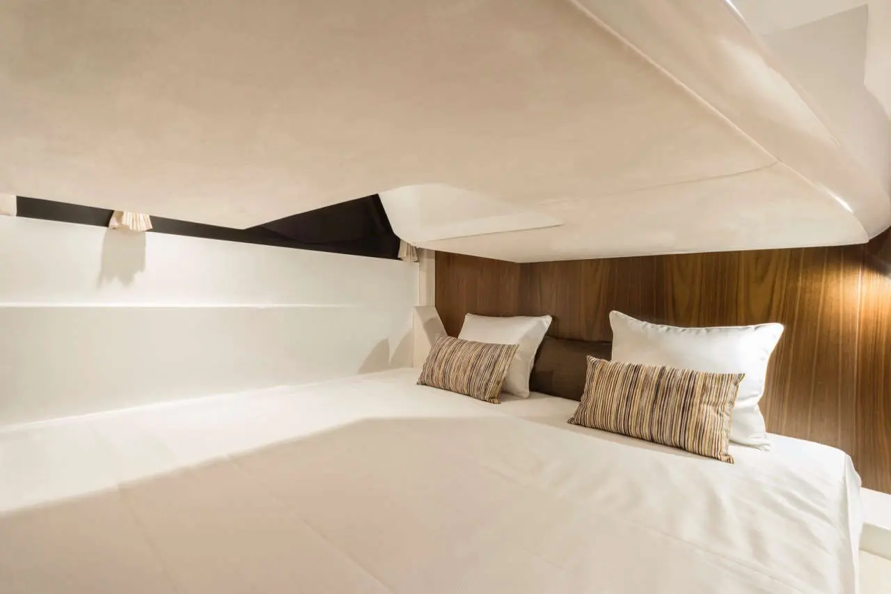 Modern boat interior with a double bed, two decorative cushions, and warm wooden accents under soft lighting.