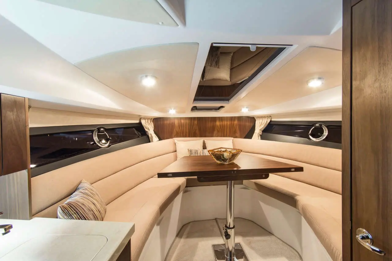 Cozy interior of a yacht featuring a U-shaped tan seating area, a wooden table, and decorative bowl, illuminated by soft lighting.