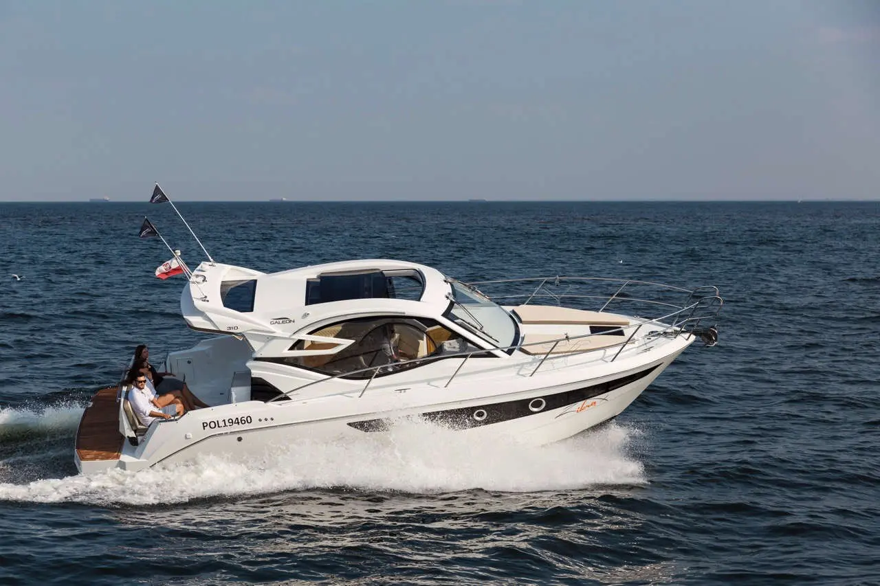 A white luxury boat, labeled POL19460, speeds through the water with two people enjoying the ride.