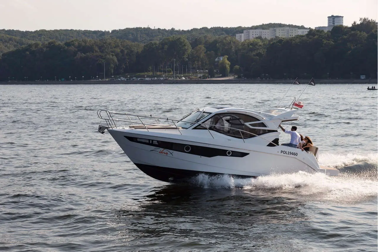 A modern motorboat with the number POL19460 speeds across a lake, with passengers enjoying the ride against a scenic backdrop.