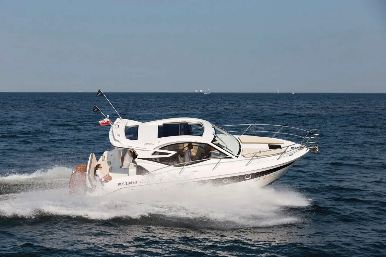 A sleek white motorboat speeds through the sea, creating a splash, with a passenger seated at the rear.