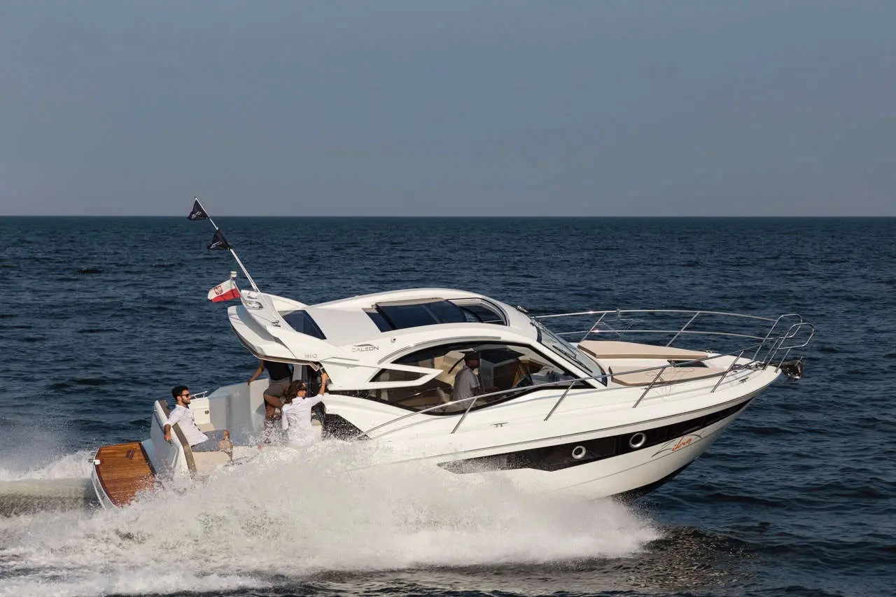 A sleek white motorboat speeds across the ocean, with passengers enjoying the ride under clear skies.