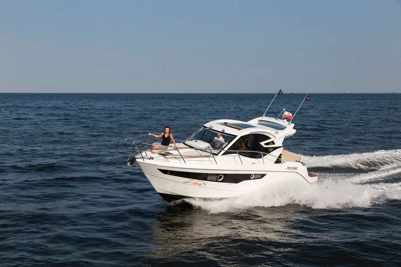 A white motorboat navigates blue waters with a woman enjoying the ride and a man steering, displaying a carefree atmosphere.
