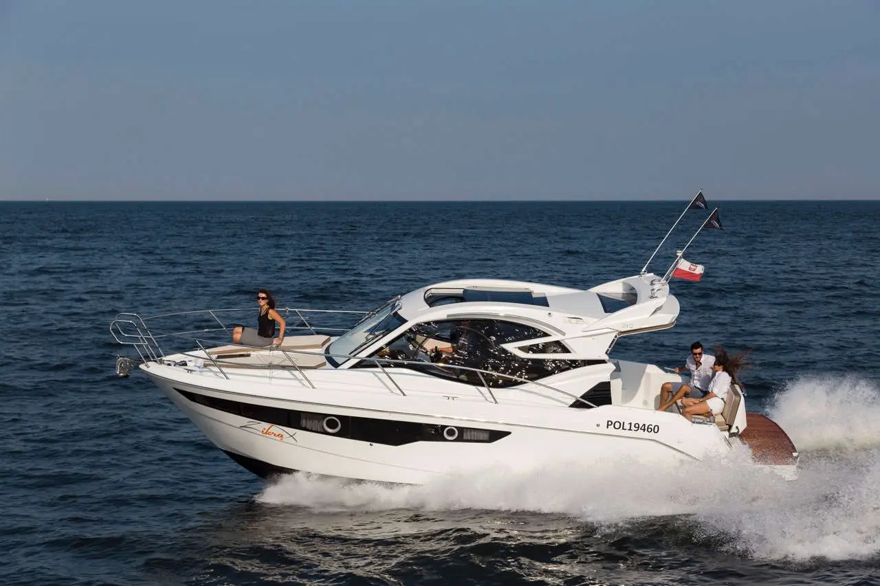 A white motorboat speeds across the sea, with two people enjoying the ride, one sitting on the bow, and others on board.