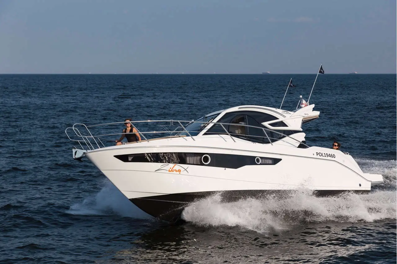 A sleek white motorboat named 'Zibra X' cuts through blue waters, with two people enjoying the ride, one at the helm.