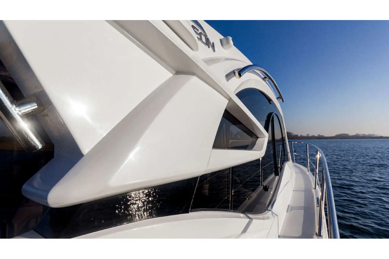 Close-up of the sleek side of a luxury yacht, reflecting sunlight over calm water against a clear blue sky.