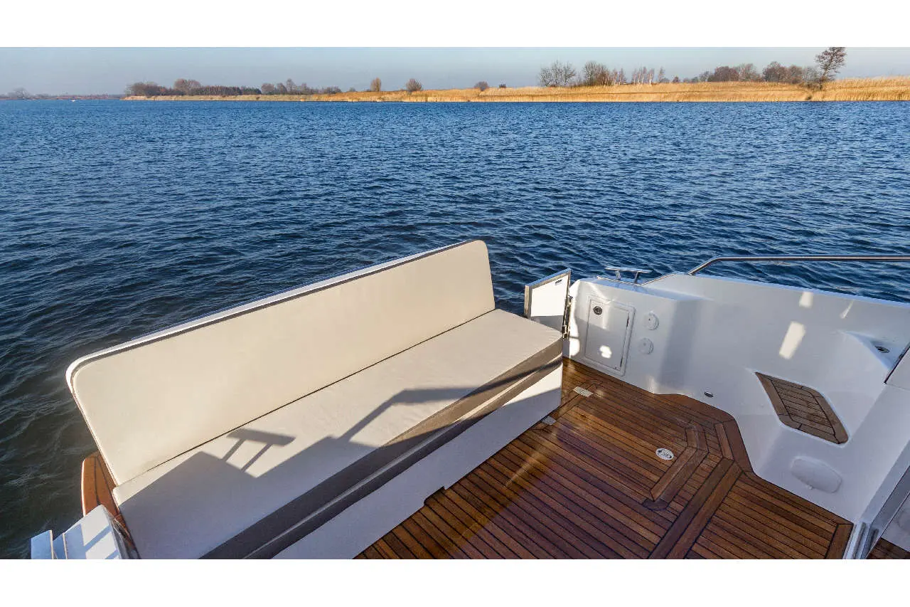 A sunlit boat deck features a plush seating area with water and reeds visible in the background, ideal for relaxation.