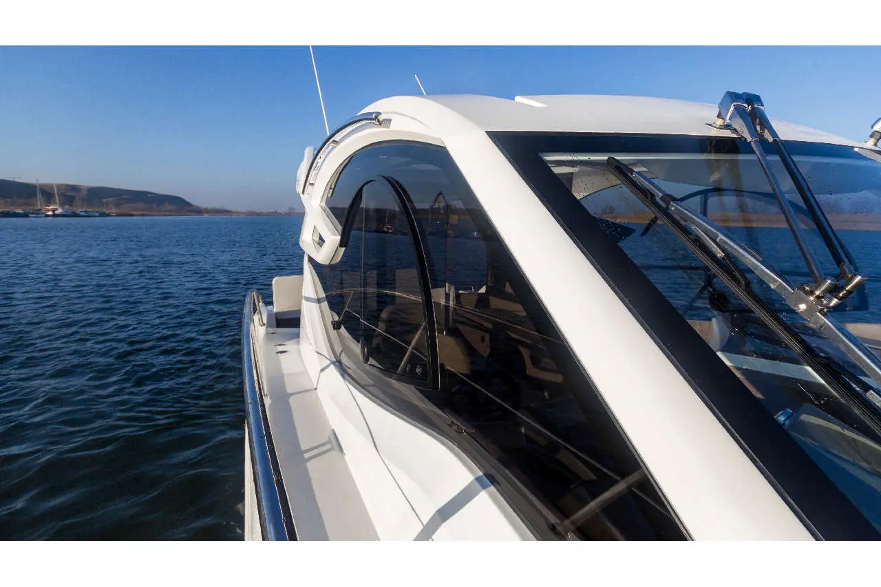 View of a sleek white boat with a modern windshield, reflecting water and blue sky, anchored by a calm shoreline.