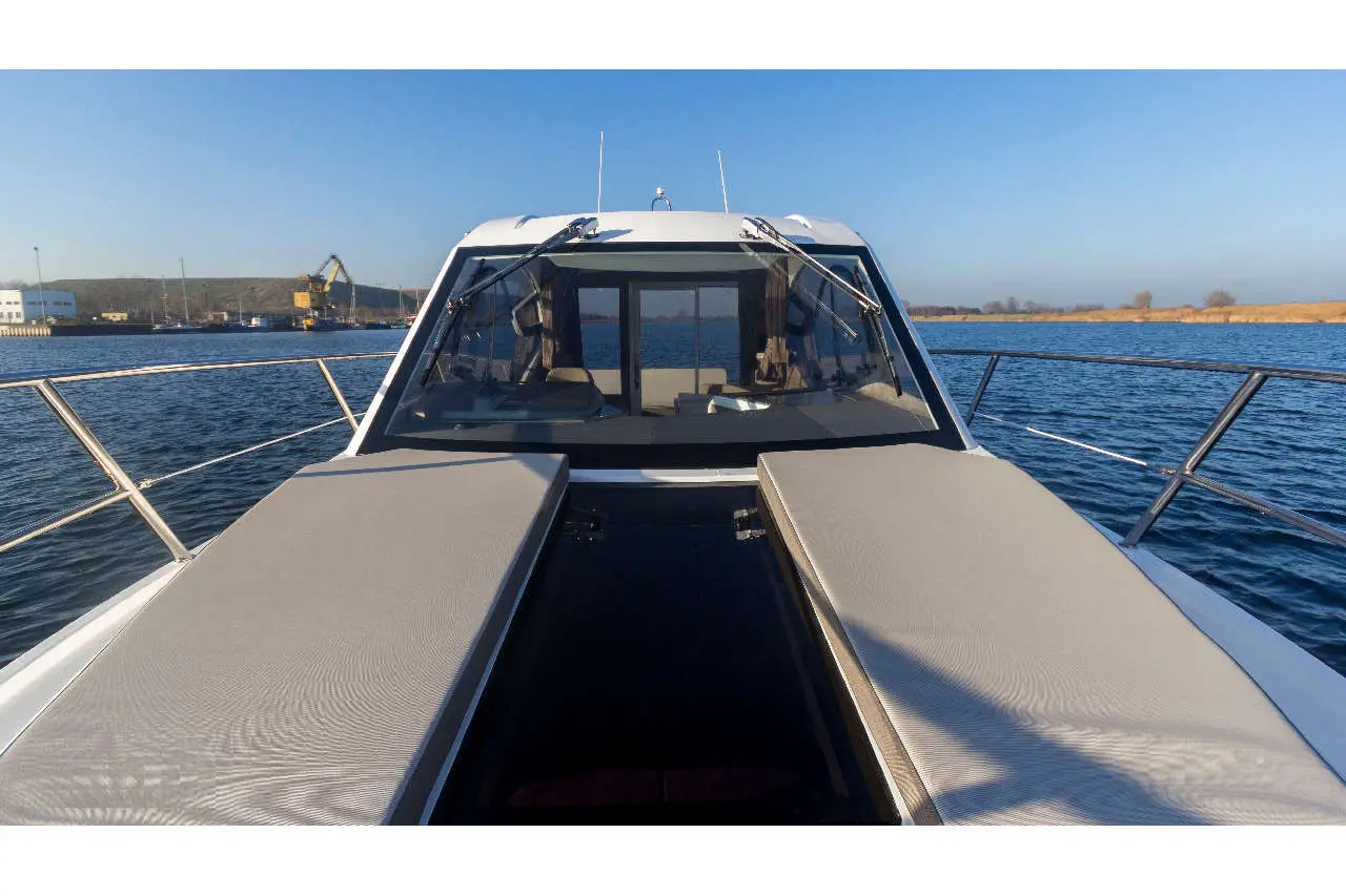 View from the bow of a boat featuring padded seating, overlooking blue water with a dock and crane in the background.