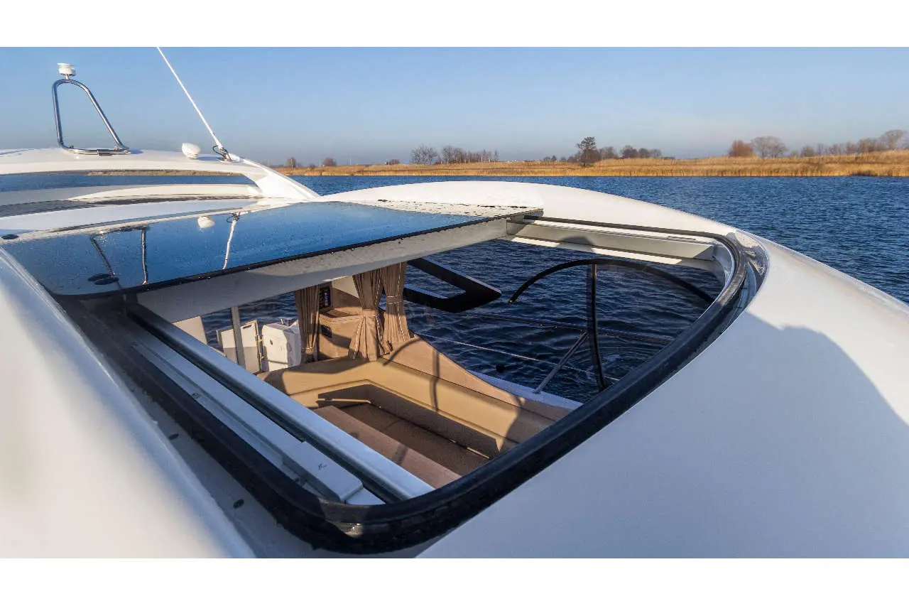 View of a boat's open roof hatch revealing a stylish interior with soft seating, set against a scenic water backdrop.