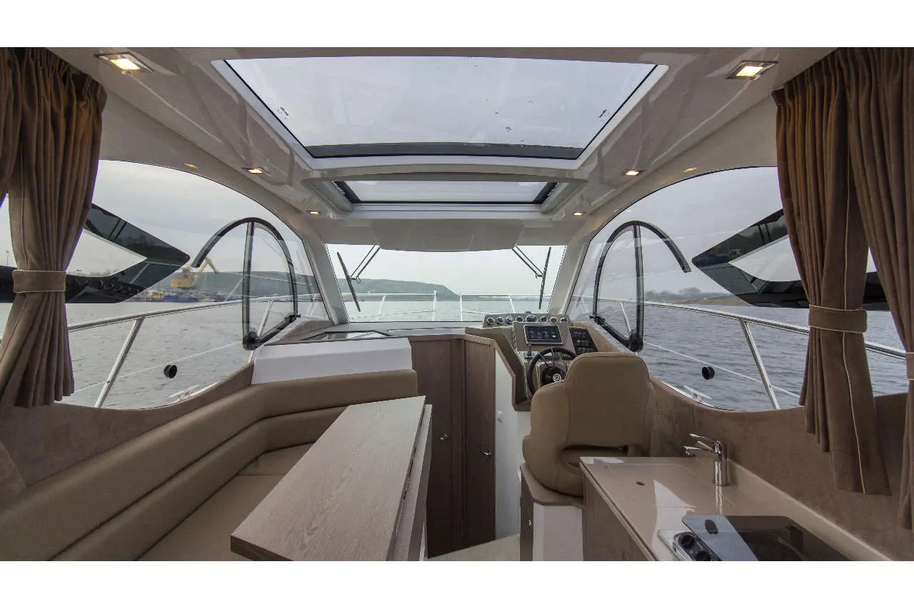 Interior view of a luxury motorboat showing the helm, seating area, and panoramic windows overlooking the water.