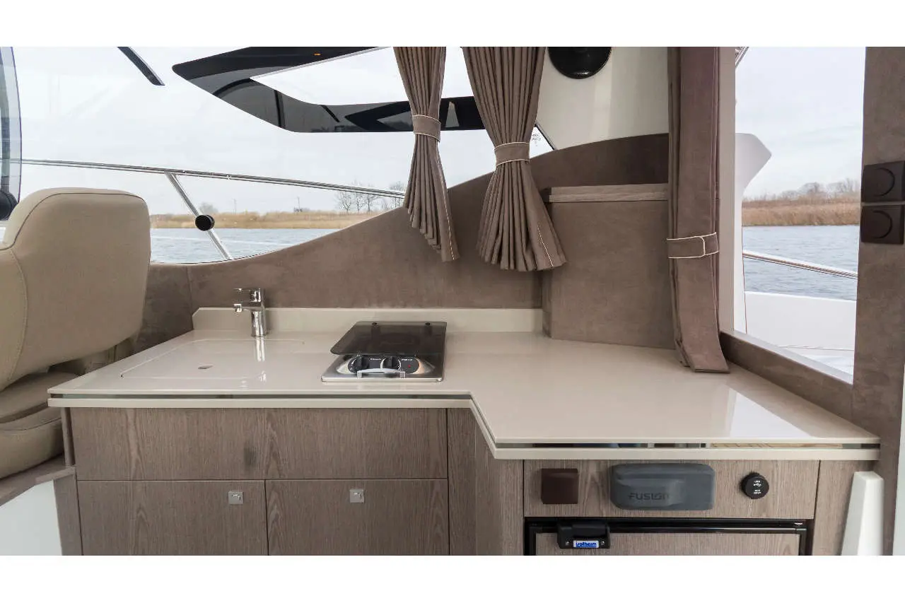 Modern boat interior featuring a kitchenette with a sink, stove, and cabinets, plus water views through large windows.