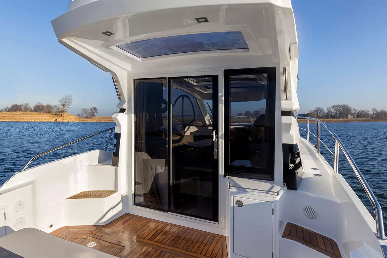 Luxurious boat interior with sliding glass doors, wooden decking, and panoramic windows overlooking a tranquil water view.