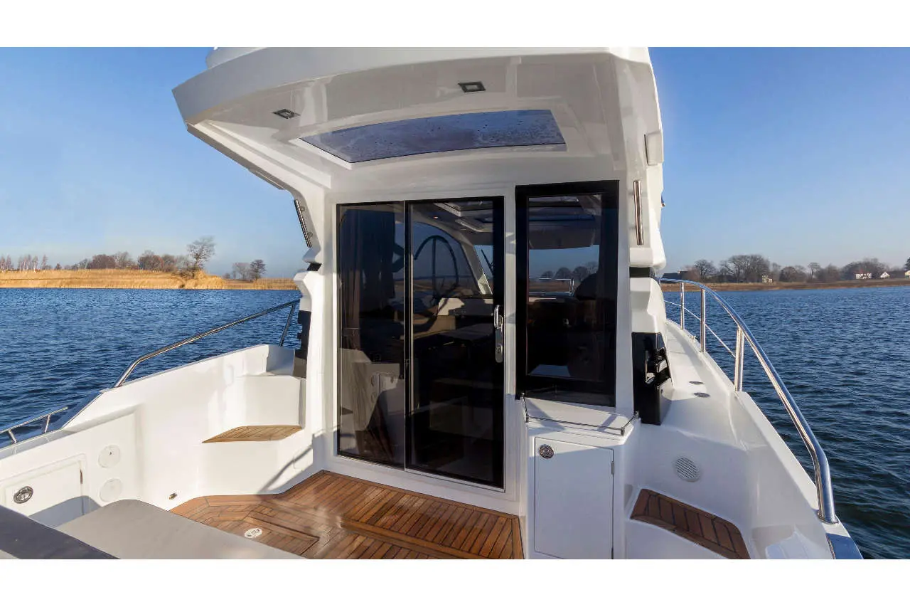 A modern boat deck featuring a glass door, wooden flooring, and scenic water views under a clear blue sky.