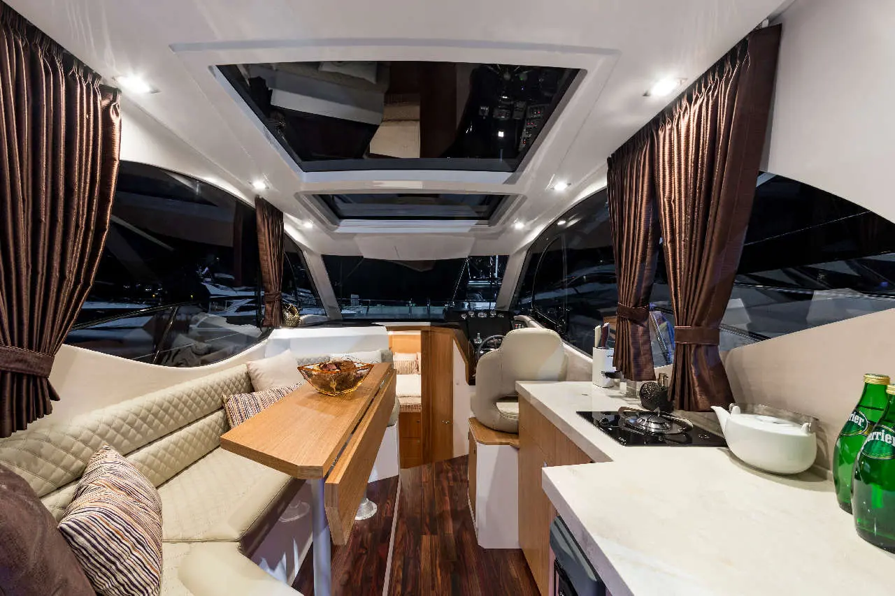 Interior of a modern yacht featuring a kitchen area, dining table, plush seating, and large windows with curtains.