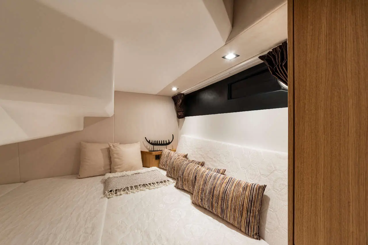 Cosy bedroom with white bedding, striped pillows, and a wooden bedside table under soft lighting and minimalistic design.