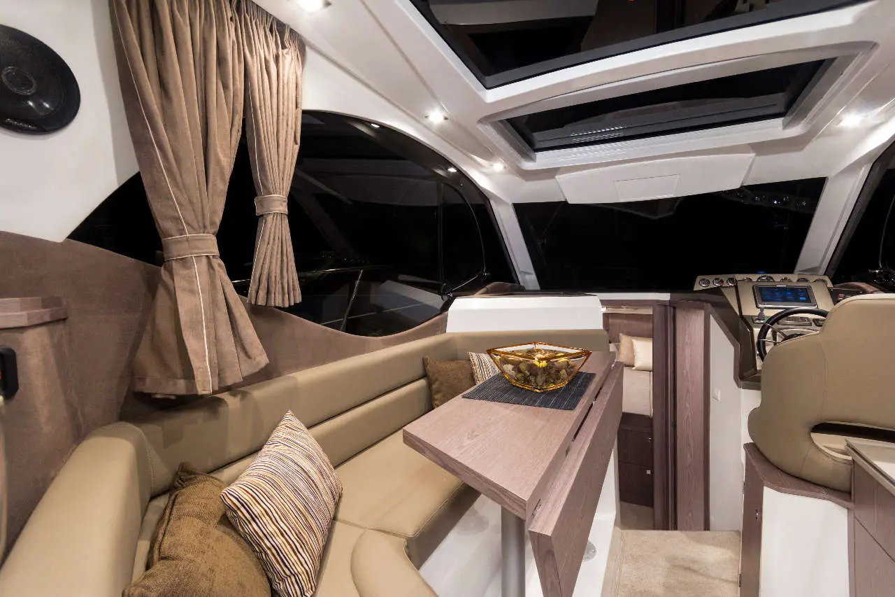 Luxurious yacht interior featuring beige seating, decorative pillows, a wooden table, and elegant curtains, illuminated softly.