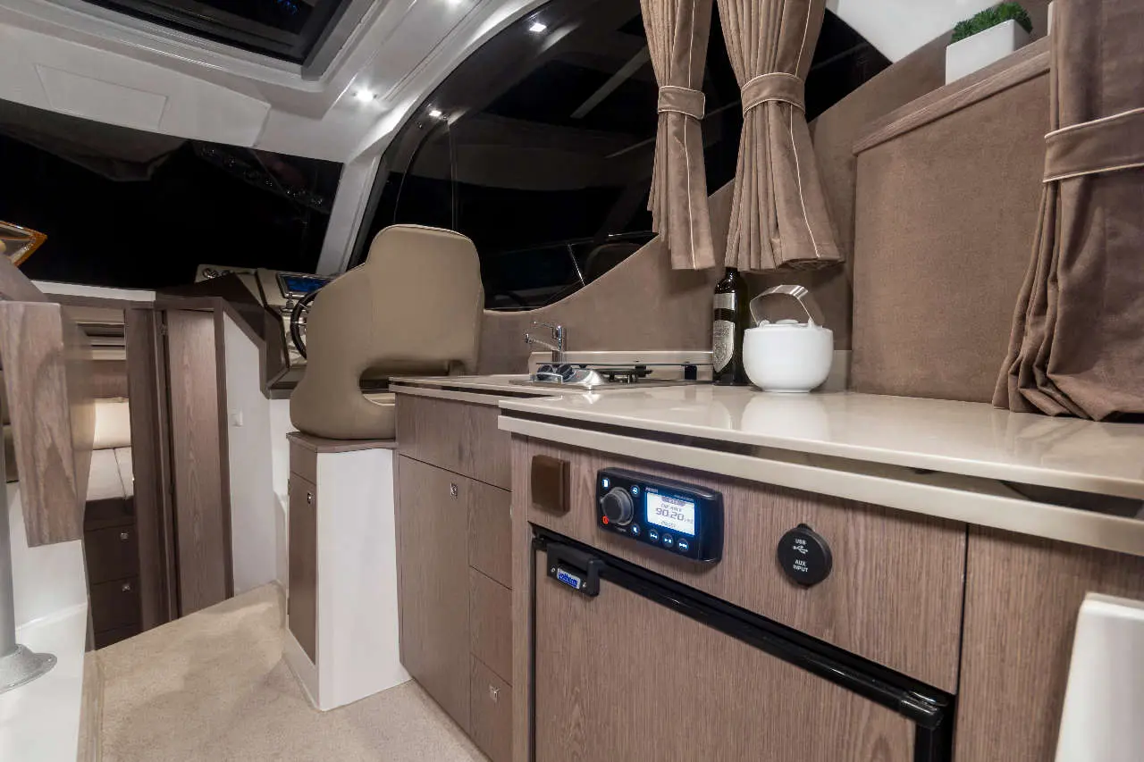 Modern boat interior featuring a galley with a sink, stovetop, cabinet space, and a beige captain's chair.