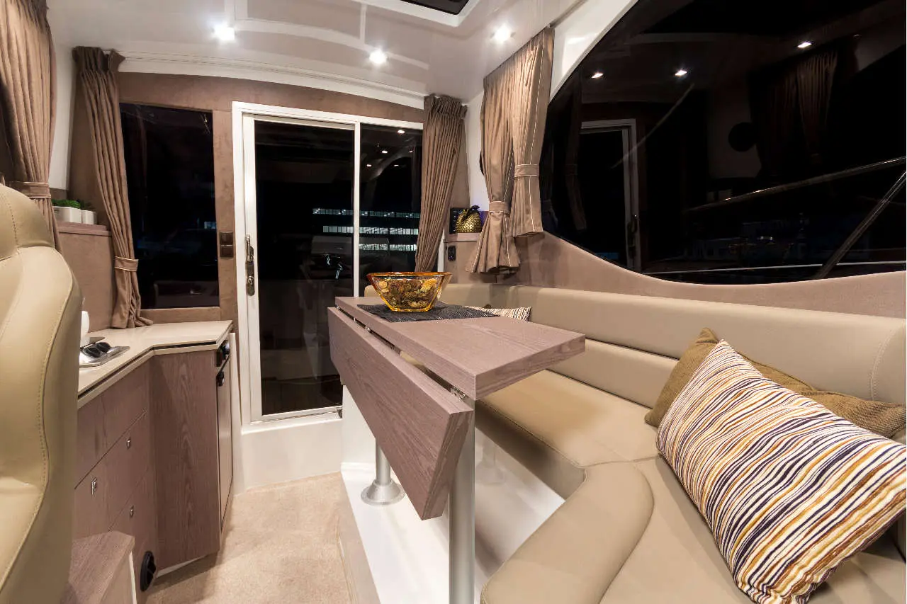 Luxurious boat interior featuring a beige sofa, wooden table, decorative bowl, and large windows with curtains.