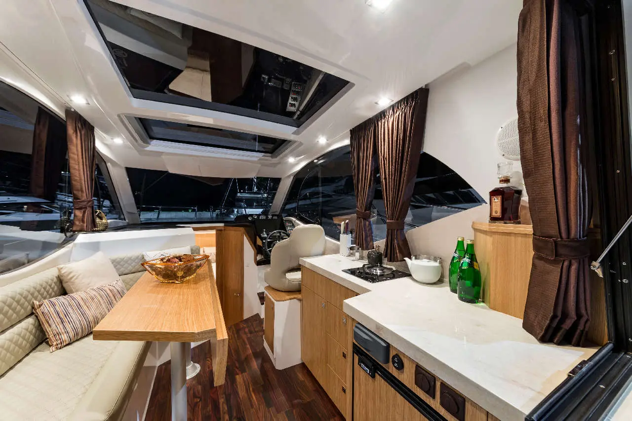 Modern yacht interior featuring a dining table, kitchenette, and ample windows with views of the marina at night.