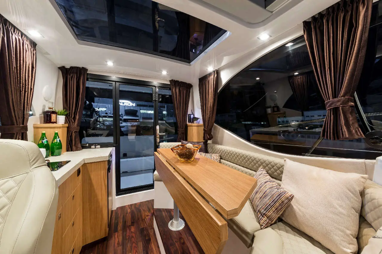 Luxurious boat interior featuring a wooden table, cushioned seating, and large windows with elegant curtains.