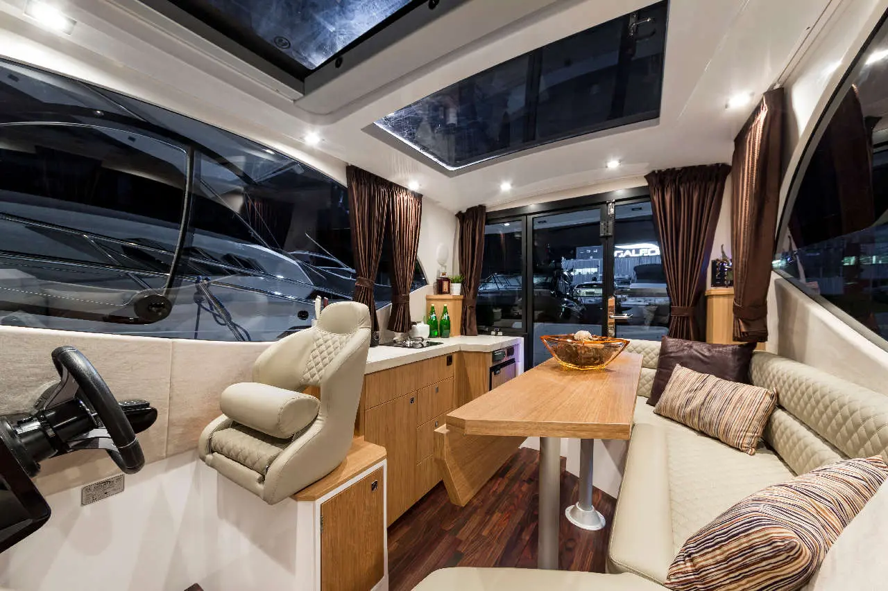 Modern yacht interior featuring a steering wheel, plush seating, wooden table, and large windows with night scenery outside.
