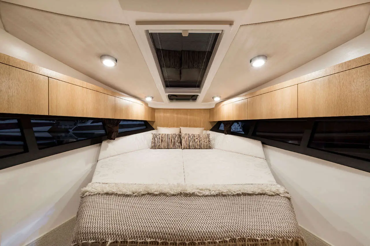 Cozy boat cabin featuring a double bed with decorative pillows, wooden cabinetry, and ambient lighting from ceiling lights.