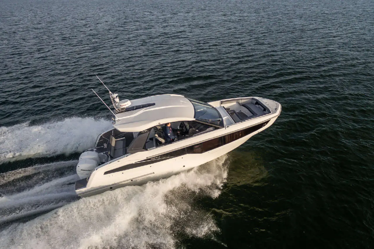 A sleek motorboat speeds across water, leaving a frothy wake, with a captain visible at the helm.
