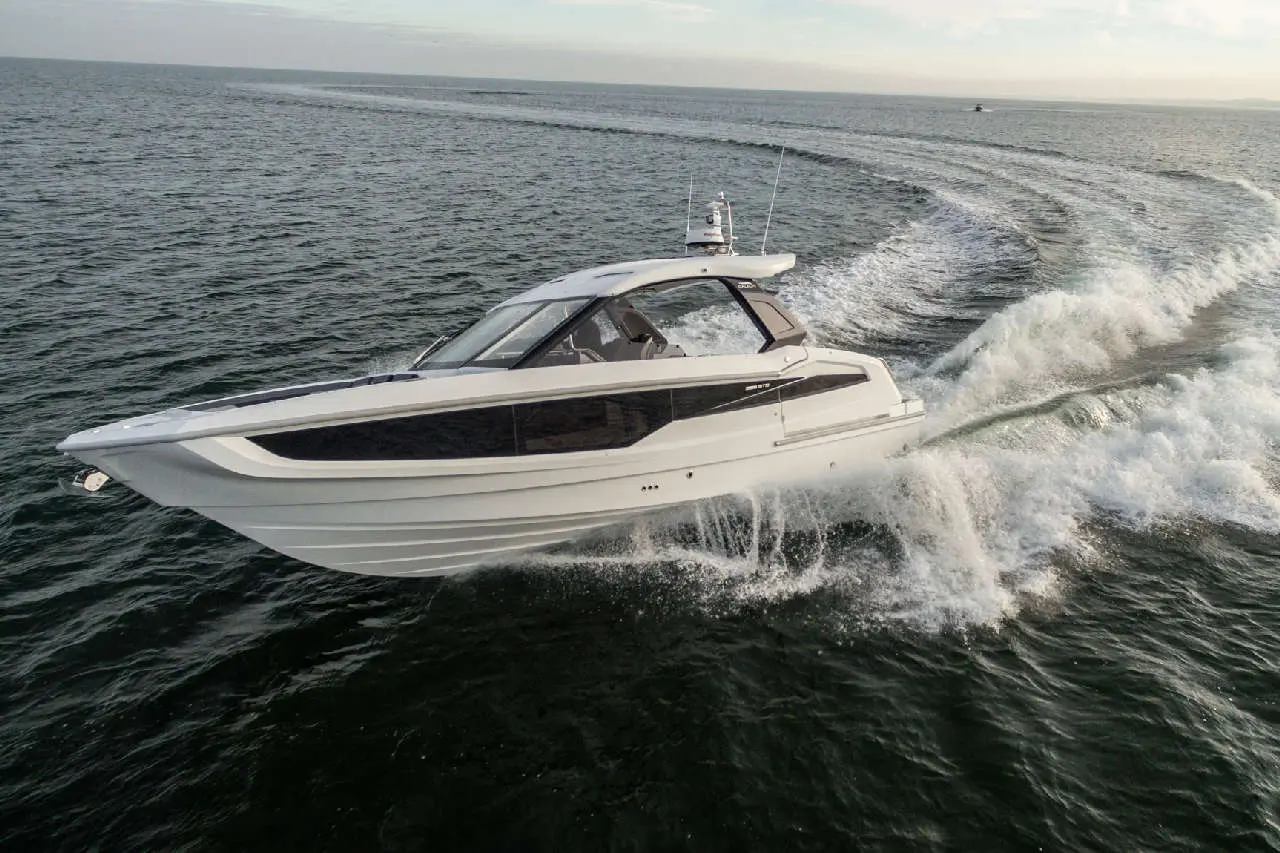 A sleek white motorboat glides across the waves, creating spray, against a calm sea backdrop under a clear sky.