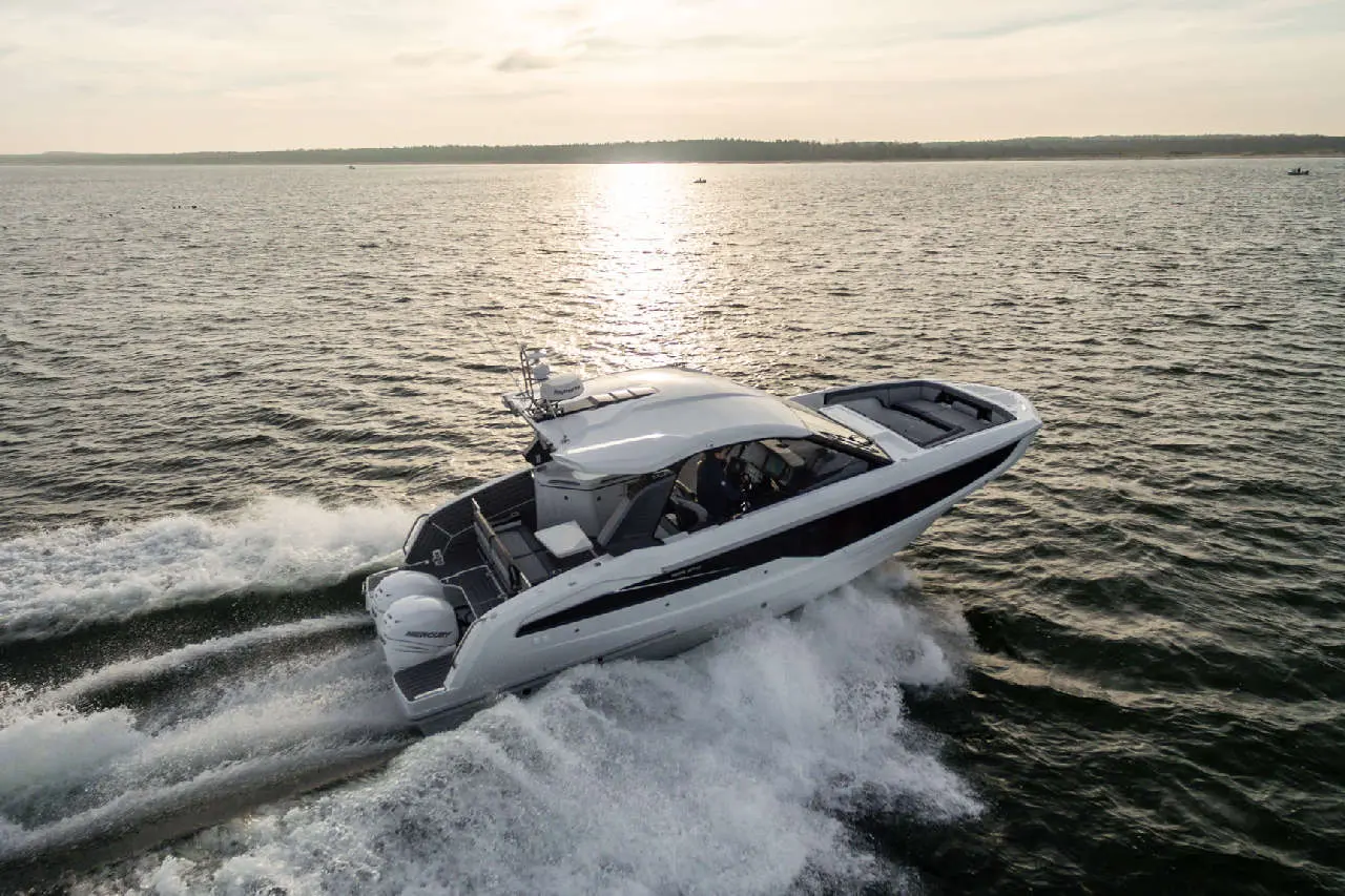 A sleek white motorboat speeds across shimmering water at sunset, creating a wake behind it.