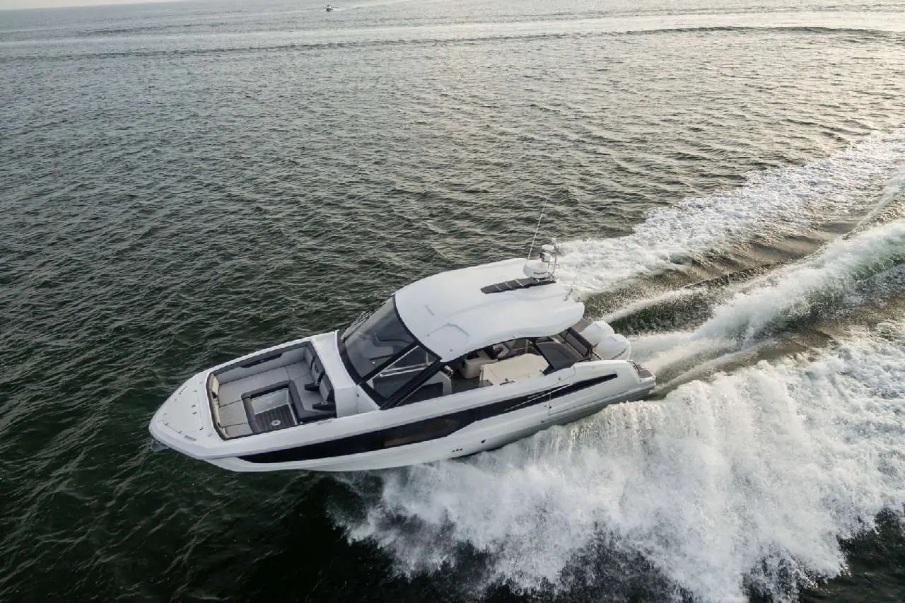A white luxury motorboat speeds across the water, leaving a frothy wake in its path under a clear sky.