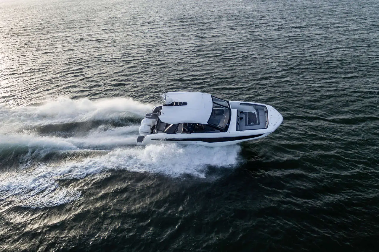 A motorboat speeding through water, causing waves, with a sleek design and a white exterior against a tranquil background.