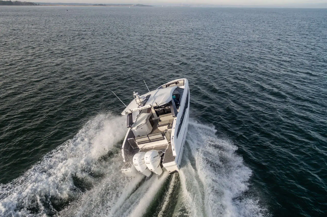 A white motorboat cruising on water, creating waves with two outboard engines visible at the stern.