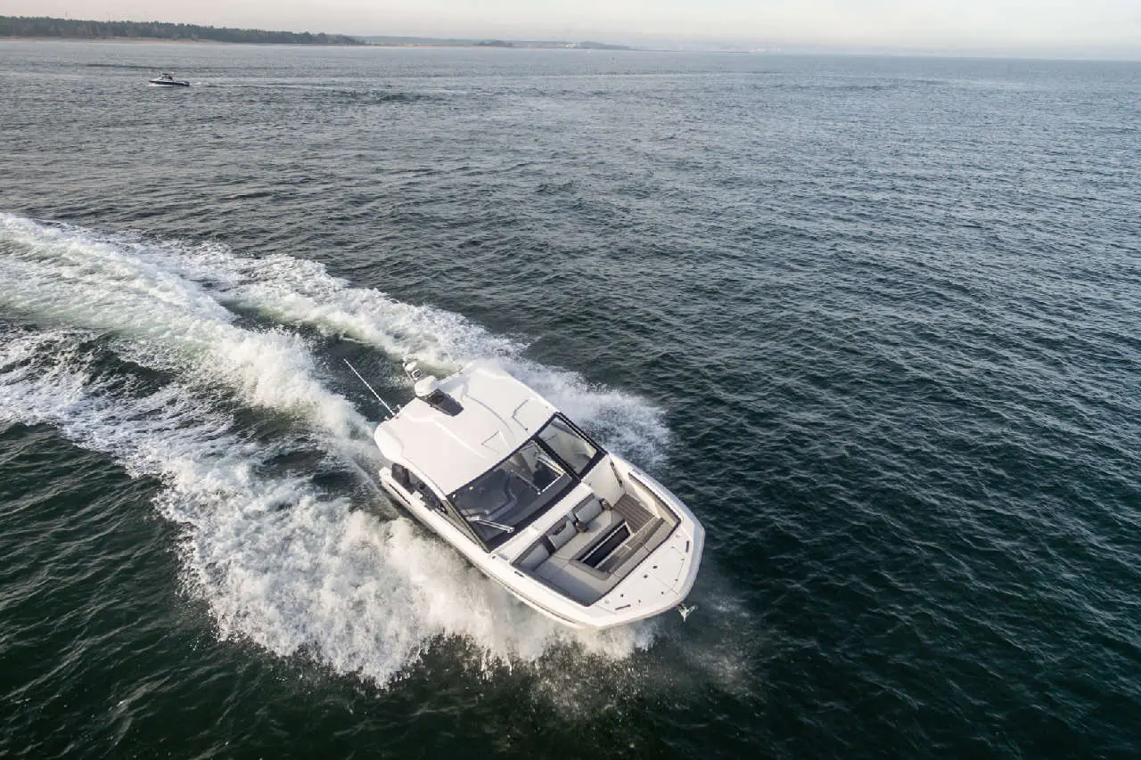 White boat creating a wake while navigating through calm water, with distant shoreline visible under a clear sky.