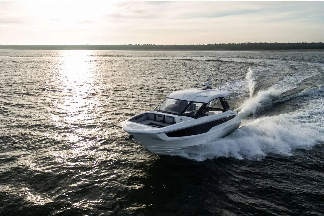 A white motorboat speeds across a sunlit lake, creating waves against the tranquil water and distant tree line.