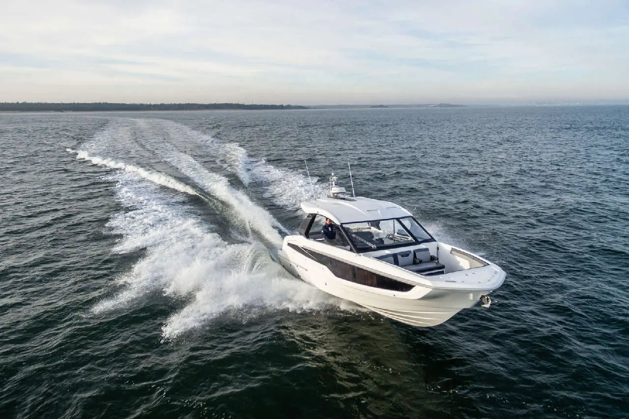 A white motorboat speeds across the water, leaving a wake behind it, under a clear sky.