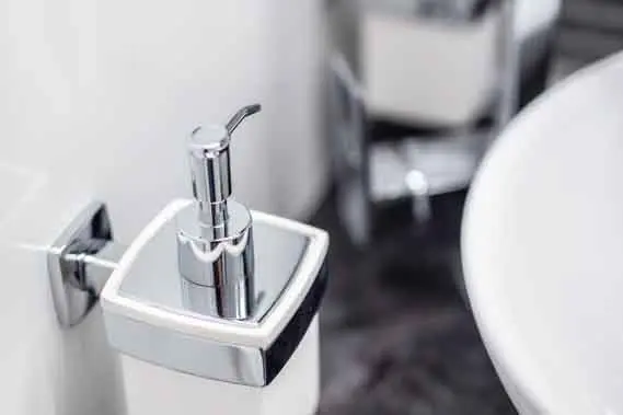 Silver pump dispenser for liquid soap next to a white sink in a modern bathroom setting.