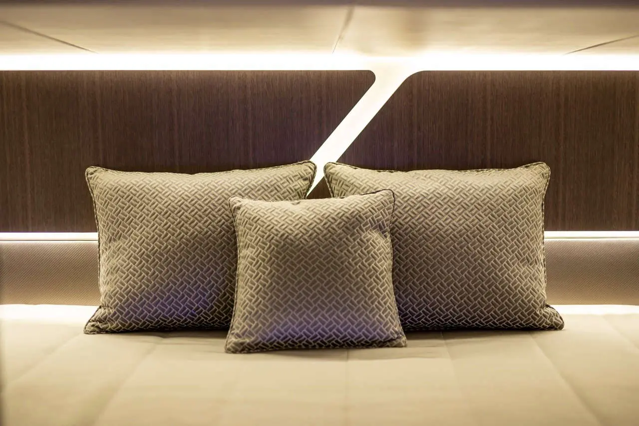 Cluster of three decorative cushions on a stylish bed, with soft lighting illuminating a sleek wooden headboard.