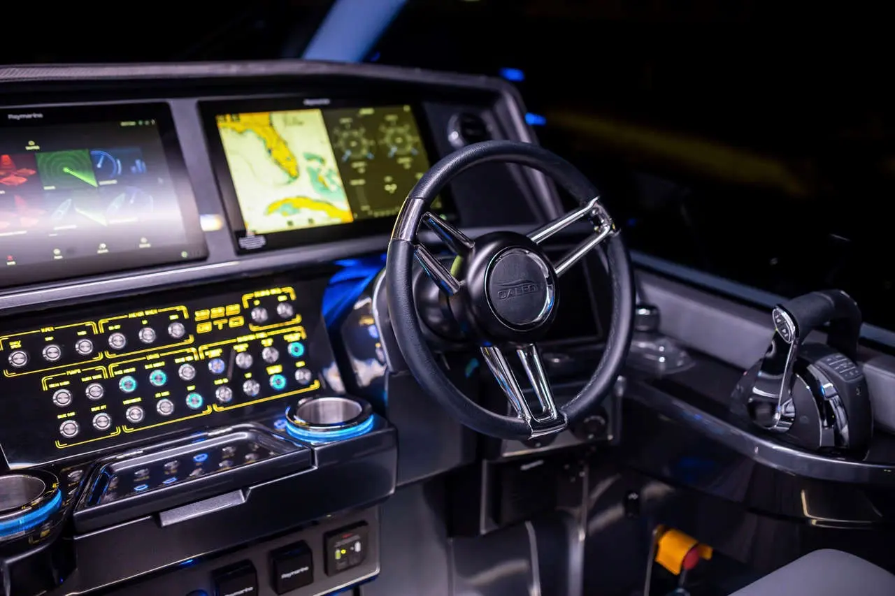 Modern boat cockpit with a steering wheel, touchscreen displays, and control buttons. Illuminated interface and maps visible.