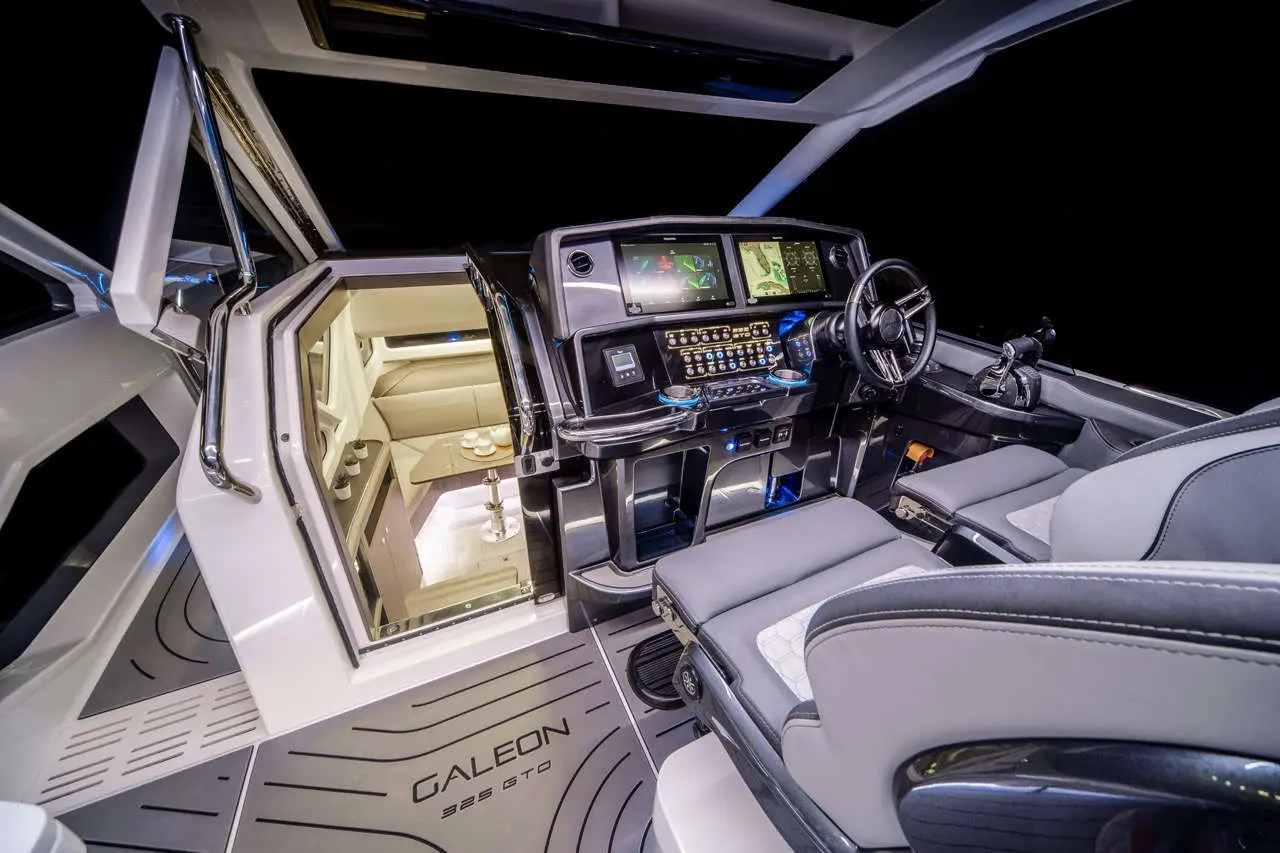 Luxury yacht interior featuring a modern helm with screens, controls, and an open door leading to a lounge area. 