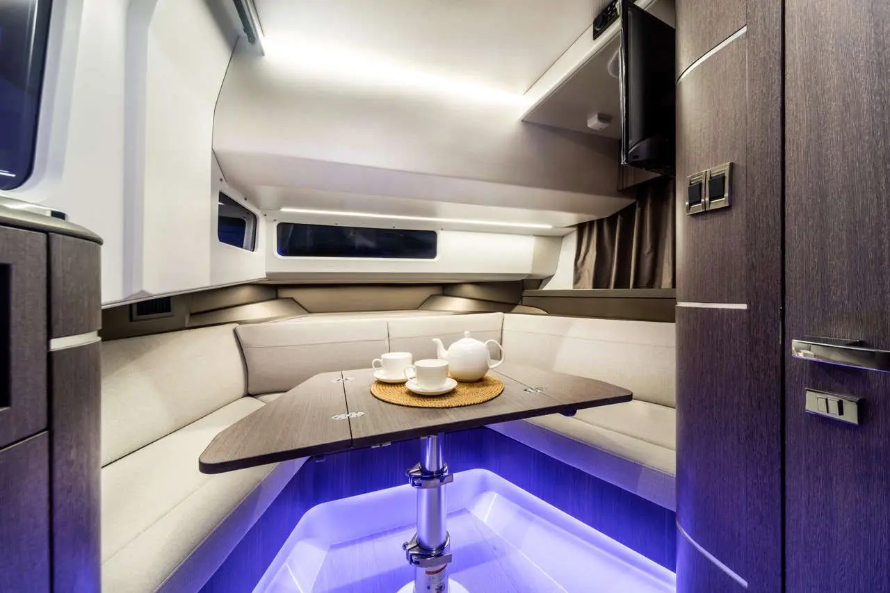 Modern interior of a boat with a round table set for tea, featuring a teapot and cups, illuminated by blue lighting.