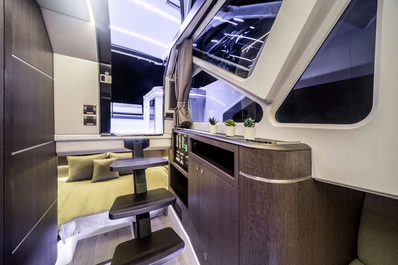 Modern boat interior featuring a compact sleeping area, kitchenette, and large windows with ambient lighting and plants.