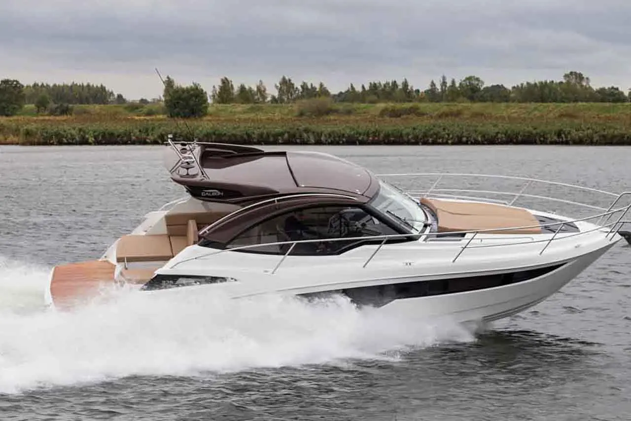A sleek motorboat cruising at high speed on a waterway, creating a spray of water with green countryside in the background.