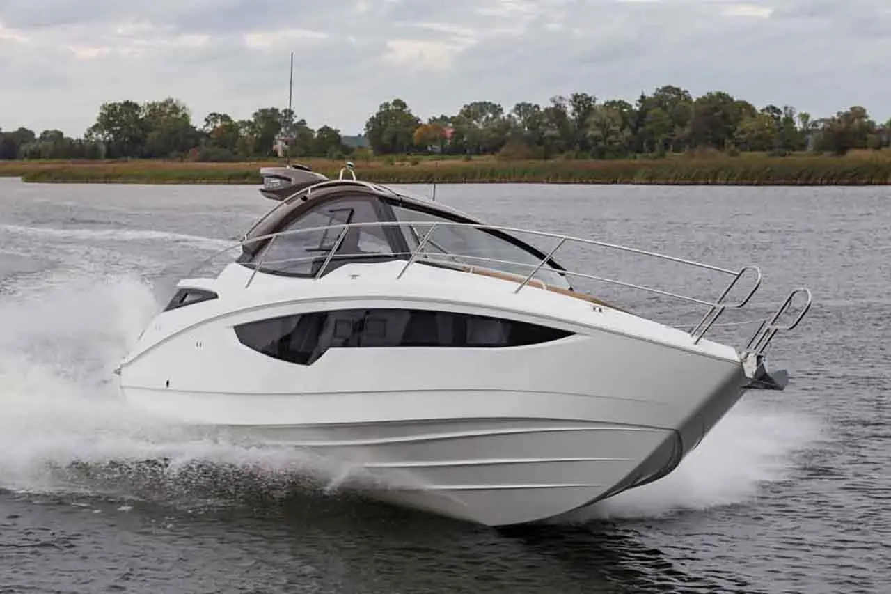 A sleek white motorboat speeds through the water with a calm, green landscape in the background.