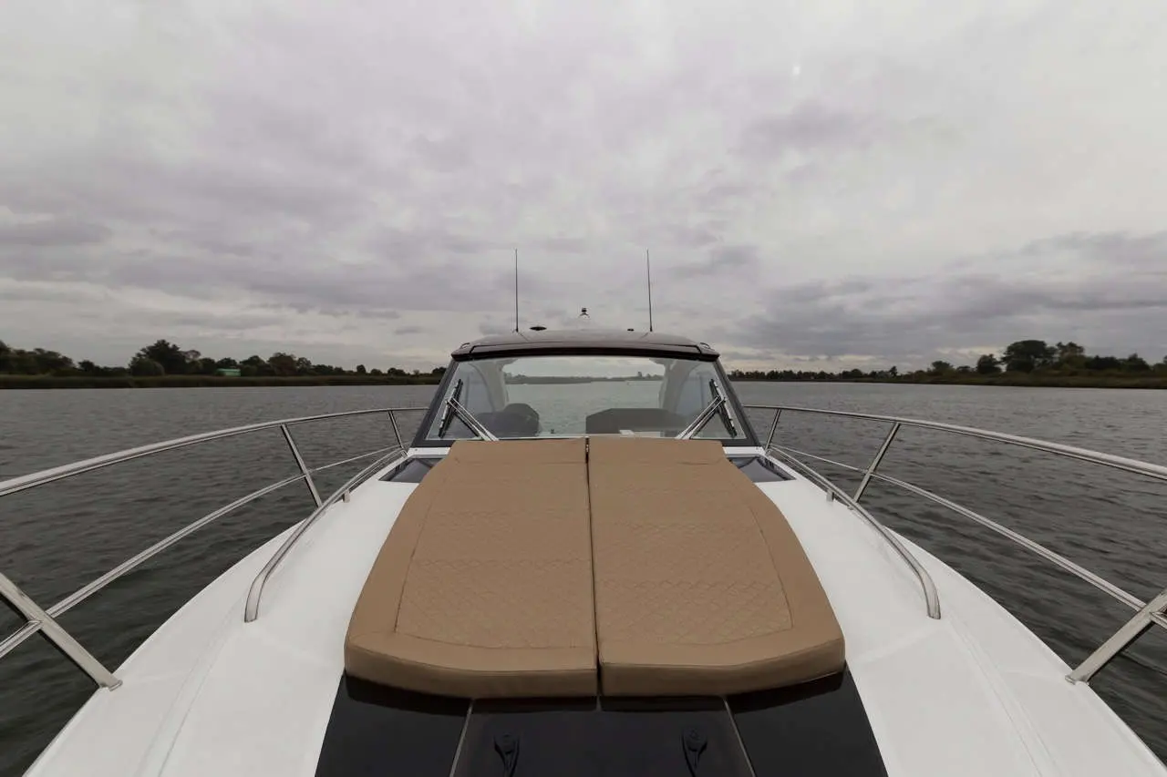 Bow view of a boat on the water, featuring a tan sun pad and cloudy skies in the background.