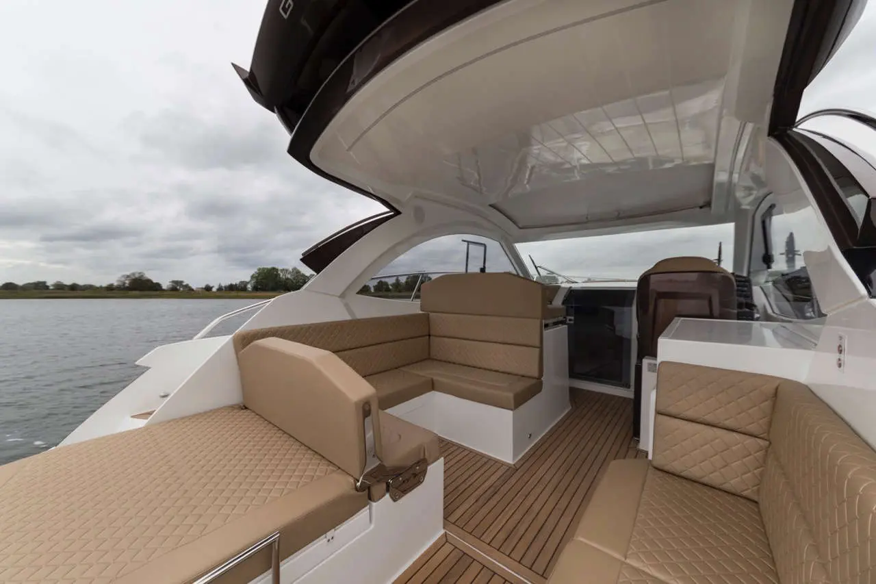 Luxury boat interior with spacious seating area, wooden flooring, and a panoramic view of the water under a cloudy sky.