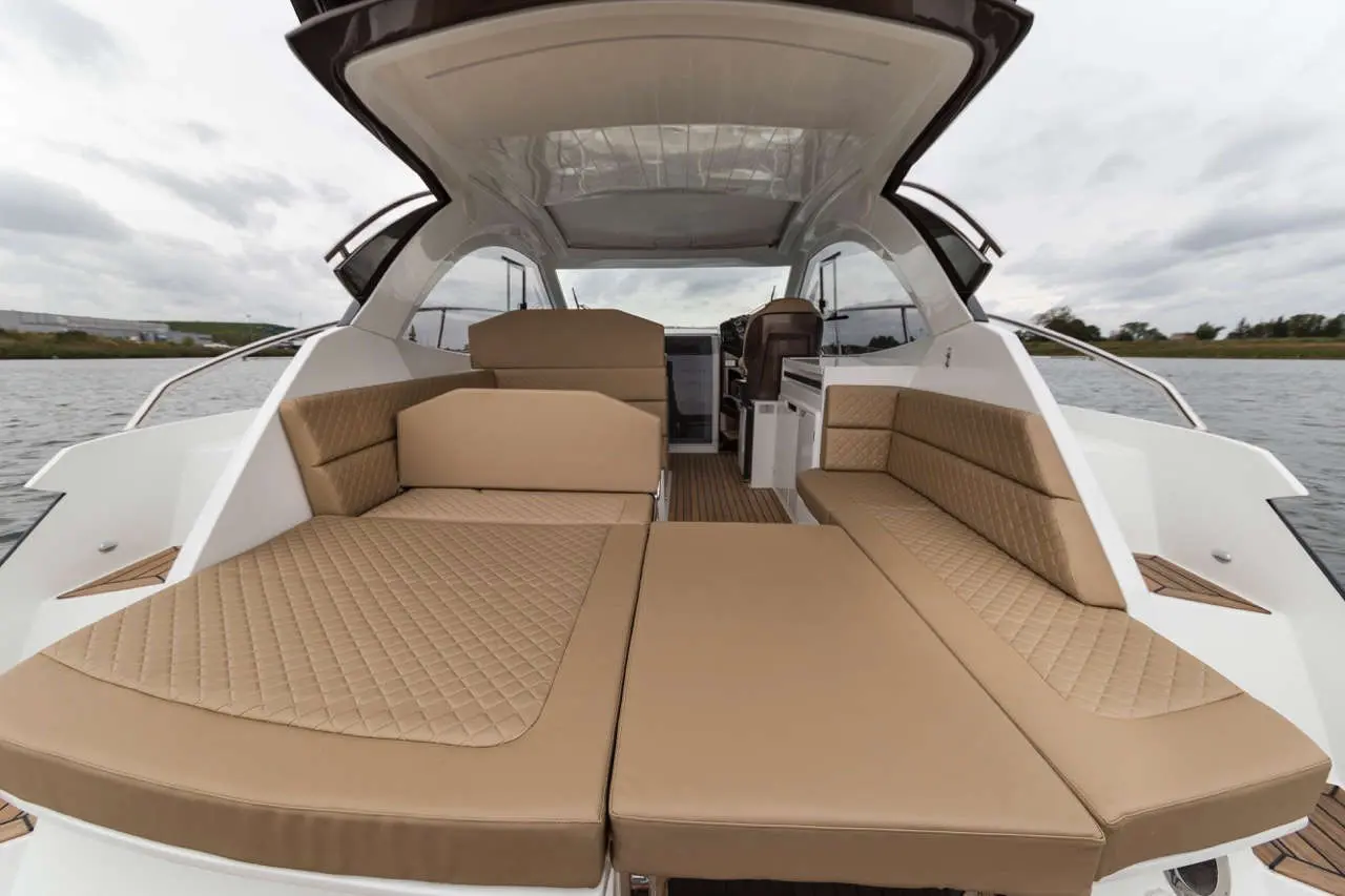 Modern boat interior featuring stylish beige seating and cushions, with panoramic views of water and cloudy skies.