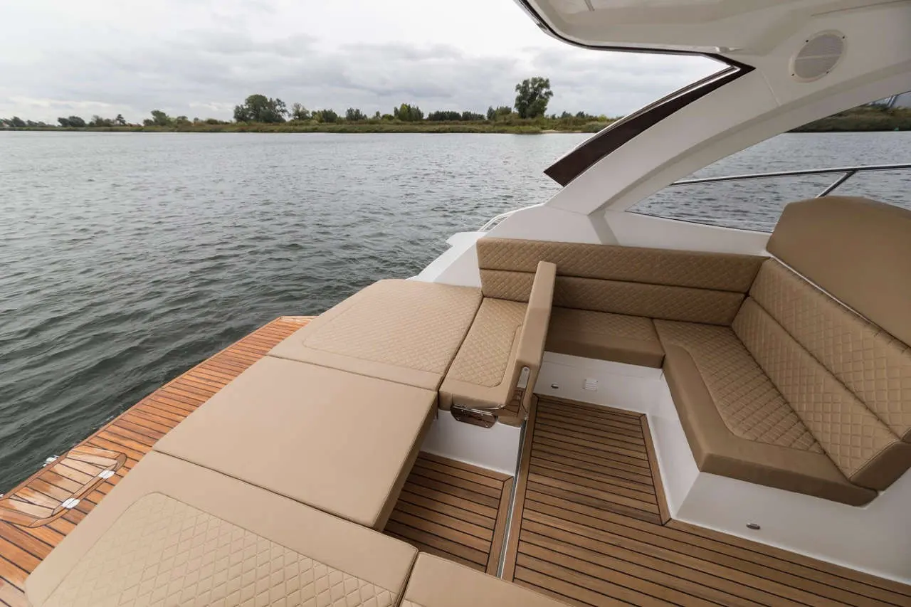 Luxurious boat seating area on water, featuring tan cushions and polished wooden deck, under a cloudy sky.