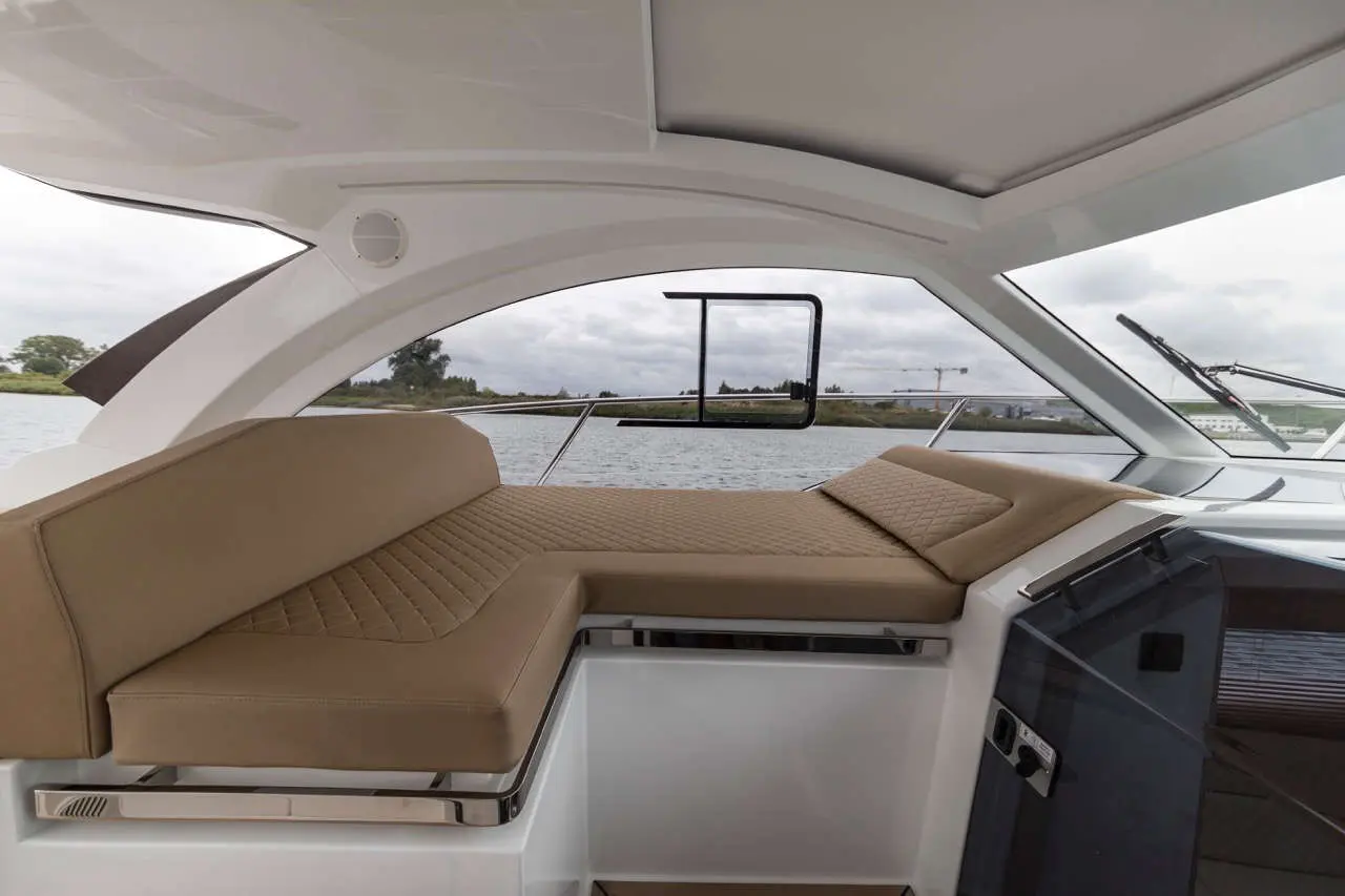 Luxurious boat interior featuring a cozy, tan cushioned seating area with a view of the water and cloudy sky outside.